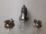 a silver tea pot and two silver cups on a glass table