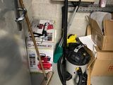 a vacuum in the corner of a room next to boxes and a broom