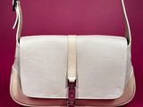 the white and beige purse is sitting on a pink surface