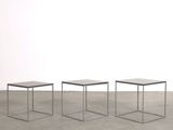 three small tables sitting on top of a cement floor next to a white wall