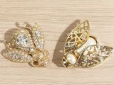 pair of gold tone brooches with pearls and diamonds on a wooden surface