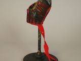 un petit chapeau rouge posé sur un support noir, orné d'un ruban rouge