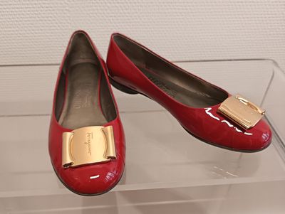une paire de chaussures rouges ornées de boucles dorées, exposée dans une vitrine