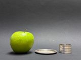 a green apple next to a silver coin on a table