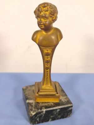 gold statue of a child on a marble base on a blue surface