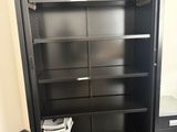 une bibliothèque en métal noir avec des tiroirs et des étagères dans une pièce