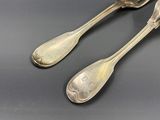 une paire de cuillères anciennes en argent et un repose-cuillère posés sur une table