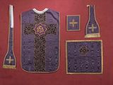 un gilet violet orné d'une croix, posé à côté d'autres objets sur une surface rouge