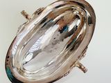 an oval silver plate with a handle on a white surface