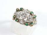 a close up of a diamond and emerald ring on a white surface
