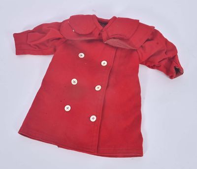 un manteau rouge de poupée orné de boutons blancs, posé sur une surface blanche