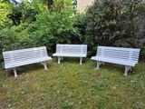 three white benches sitting in the grass near some bushes