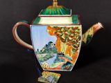 a teapot with a painting on it sitting on a table