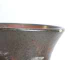 a brown vase sitting on a table with a white wall in the background