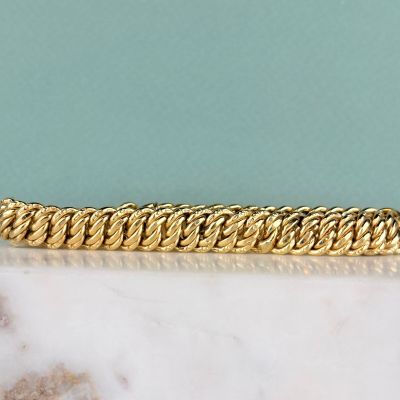 un gros plan d'un bracelet à chaîne en or posé sur une surface en marbre
