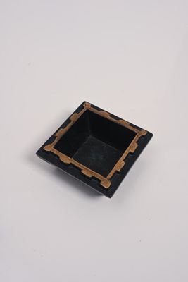 un petit cendrier carré noir et doré posé sur une table blanche