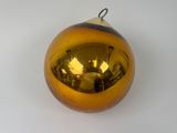 une boule de Noël jaune accrochée à un mur blanc, avec le reflet d'une personne dans le miroir
