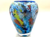 un vase en verre aux couleurs vives posé sur une surface blanche, avec une lumière en arrière-plan