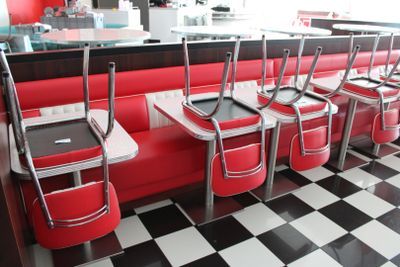 Plusieurs chaises rouges sont alignées dans un snack-bar au sol carrelé de carreaux noirs et blancs.