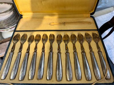 des couverts rangés dans un coffret posé sur une table, à côté d'une pile d'assiettes