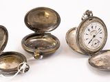 Plusieurs montres de poche anciennes en argent sont posées sur une surface blanche