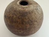 un vase marron percé d'un trou, posé sur une surface blanche
