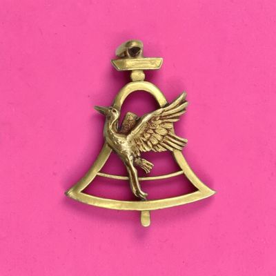 une cloche en laiton surmontée d'un oiseau, sur fond rose