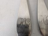 three silver spoons with initials on them sitting next to each other