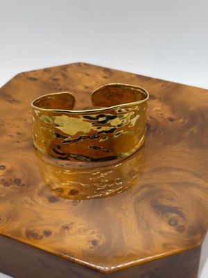 bracelet manchette plaqué or posé sur un coffret en bois, sur fond blanc