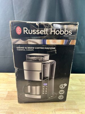 une boîte contenant une cafetière Russell Hobbs posée sur une table en bois