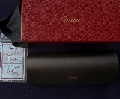 une boîte rouge ornée d'un logo doré, à côté d'une paire de lunettes