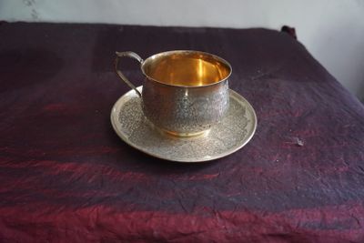 une tasse et une soucoupe argentées posées sur une nappe violette