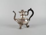 une théière ancienne en argent, dotée d'une anse noire, posée sur une table