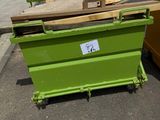 une benne verte posée sur un parking, à côté d'un tas de bois
