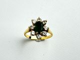 a close up of a ring with a green stone surrounded by diamonds