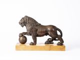 statue en bronze représentant un lion tenant une balle, posée sur un socle en marbre
