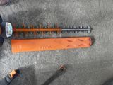 an orange corded hedger sitting on top of a cement floor next to a pair of scissors
