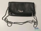 un sac à main en cuir noir orné d'ailes argentées, posé sur une table