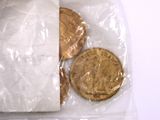 a gold coin in a plastic bag next to a penny