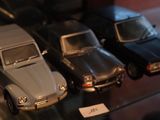 Plusieurs petites voitures sont alignées sur une étagère en verre dans une vitrine.