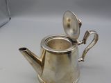 an antique silver teapot with a spoon on a white surface