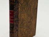an old book with a brown cover sitting on a white surface