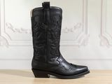 un gros plan sur une paire de bottes de cow-boy noires posées sur une table en bois