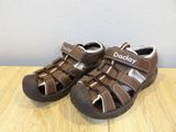 baby boy ' s brown sandals on a wooden table with a wall in the background