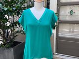 un haut vert posé sur un mannequin devant une plante en pot