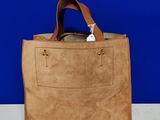 Sac fourre-tout beige à anses en cuir posé sur une table blanche