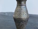 un vase en argent posé sur une table, avec un mur blanc en arrière-plan