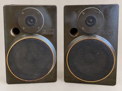 two black speakers with gold trims sit side by side on a white surface