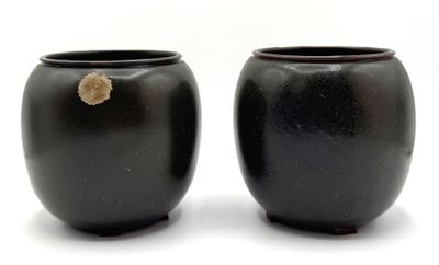une paire de vases noirs sur fond blanc, avec un petit morceau de roche au milieu