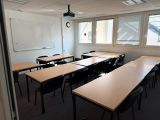 des tables et des chaises dans une salle de classe avec un tableau blanc accroché au mur